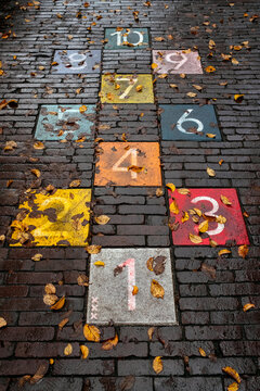 Hopscotch children's game painted on street in Amsterdam, Netherlands. Colorful tiles with numbers on a brick textured ground, fallen autumn yellow leaves around. Ranking or goal achievement activity.
