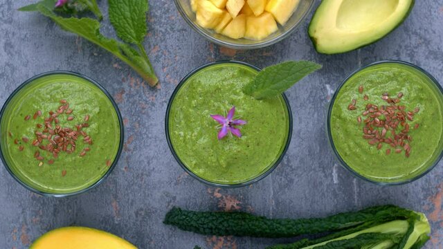 Green smoothie glasses with kale and borage leaves and ingredients. Top view of detox healthy breakfast. Table spin.