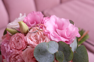 Two wedding rings of white and yellow gold on a bouquet of pink roses.
