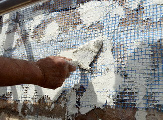 Albañil reforzando el revestimiento de un muro de ladrillo con malla de fibra de vidrio y mortero...