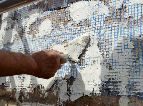 Albañil reforzando el revestimiento de un muro de ladrillo con malla de fibra de vidrio y mortero de cemento blanco