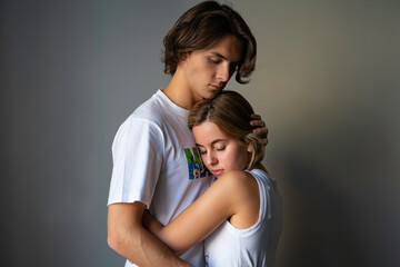 Obraz premium A young couple, a young man and a young blond woman, standing and embracing, he is holding her in hugs with closed eyes both, pressing tenderly her head to his chest, dreaming