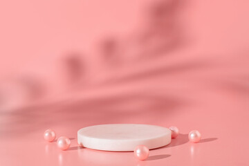White marble podium with pink pearls on the pink background with shadow of tropical plant. Podium...