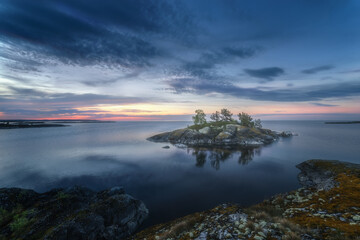 Fototapeta na wymiar Scenic evening view of a beautiful lake and a lonely rocky island. Epic blue sky. Northern picturesque and harsh nature. Ladoga skerries. Islands. Republic of Karelia. Russia.