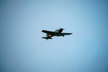 a 1950s De Havilland DHC-1 Chipmunk with a glider tow rope attached flies low overhead in a winter sky