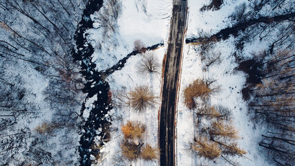 Aerial high angle view of mountain road, trees and river under the snow. Winter landscape, bird's eye view.