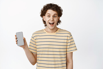Fototapeta na wymiar Enthusiastic young man showing mobile screen and smiling, demonstrating his app interface, white background