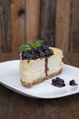Desserts. Closeup view of a slice of Cheesecake with mascarpone cheese and berries dressing, in a white dish on the wooden table.