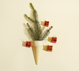 A fir tree branch in an ice cream cone with wrapped gift boxes on beige background. Retro Christmas pattern. 70s and 80s aesthetic. Minimalist concept. Copy space. Flat lay.