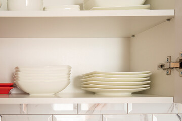 Fototapeta na wymiar White dishes plates inside open white kitchen cabinet