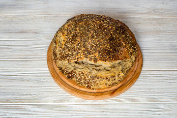 Natural loaf of yeast-free sourdough bread with sesame seeds, flax, chia, sunflower seeds, on a wooden board on the table, close-up.