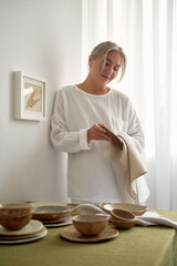 Young girl in pajamas lays the table. Natural fabrics and materials around. Cozy home. Front view.