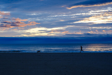 Girl with dog doing sport on the beach at sunrise