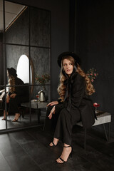Stunning woman in a trendy hat and stylish black suit in dark luxurious interior
