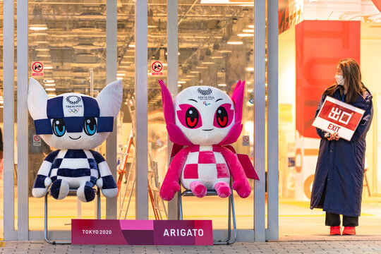 tokyo, japan - november 30 2021: Staff of the olympics official shop holding an exit panel aside the plushies of mascots Miraitowa and Someity saying arigato for the final sale at Tokyo Sports Square.