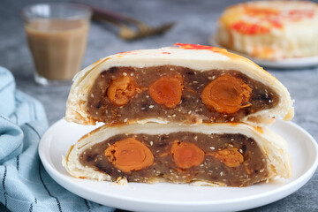 A half cutting piece of Chinese mooncake pastry in a white plate with salty egg yolk and sweet Asian squash and sesame paste filling, coffee in background. It's a flaky layers of pastry crust stuff