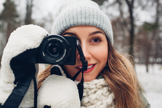 Young woman photographer takes pictures of snowy winter park using camera wearing warm clothes. Outdoor activities
