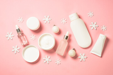 Obraz na płótnie Canvas Winter cosmetic, skincare product for woman beauty. Cream, serum, tonic with winter decorations. Top view on pink background with christmas decorations.