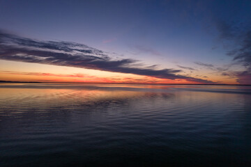 Fototapeta premium Beautiful sundown over the lake. Blue sky and pastel pink clouds during summer sunset. Mirror image of clouds in the water.