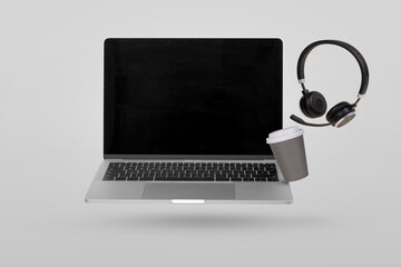 Laptop computer with empty screen, headset and paper cup with coffee levitating in the air on a...