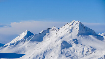 Snowy mountain peaks against the blue sky and clouds. A beautiful winter mountain landscape.