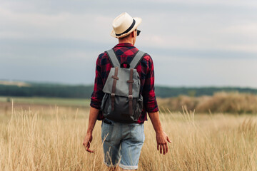 traveler with a backpack, walks in a field at sunset. Male tourist walks and enjoys the view of the beautiful nature