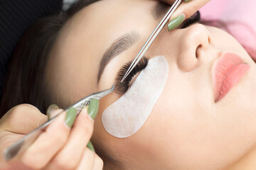 Naklejka premium Eyelash extension procedure. The master uses tweezers to apply long eyelashes to beautiful female eyes.