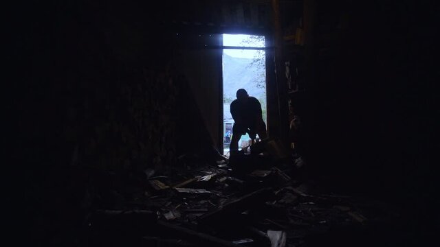 Silhouette of a man chopping wood in a barn. slow motion