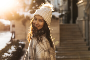 Lovely young caucasian girl walks through winter city on sunny day, turning to camera. Brown-eyed...