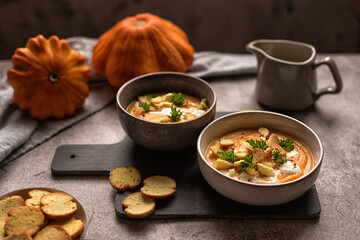autumn lunch: pumpkin cream soup with cream and crackers. serving lunch for two. photo on gray background