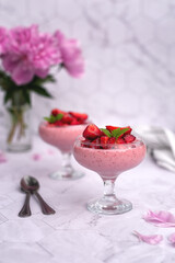 light summer dessert without baking: strawberry mousse with strawberry slices and mint. serving on a gray background with a bouquet of peonies
