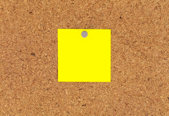 Blank yellow paper notepad reminder sticky notes on cork bulletin board. Empty space for text....
