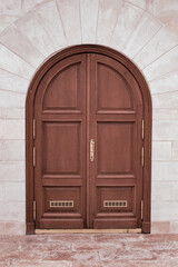 Closed wooden door with an arch in a stone white wall. Design and architecture