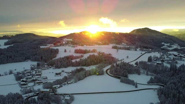A slowly moving 4K drone flight into the sunset over a beautiful winter landscape with moving clouds. Location is the Schoecklland near Graz in Austra
