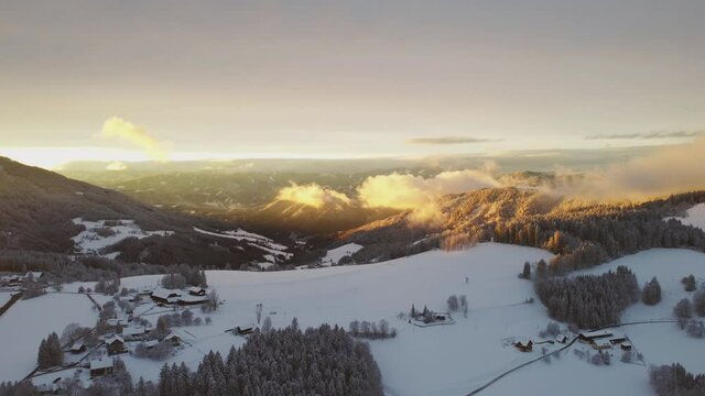 A slowly moving 4K drone flight into the sunset over a beautiful winter landscape with moving clouds. Location is the Schoecklland near Graz in Austria