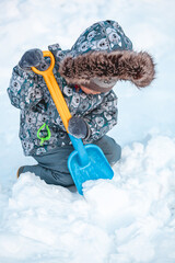 Child playing with shovel on the snow on a sunny winter day