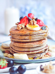 Close up of healthy oatmeal and banana pancakes top with strawberries and red grapes with walnut. Pouring with syrup with a bottle of milk in background