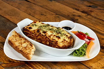 lasagna on white plate with bread and salad