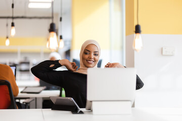 Fototapeta na wymiar African american muslim girl with hijab working on a laptop in an office..