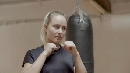 Medium shot of confident female boxer getting ready for kick. Slow motion of focused woman practicing in boxing room, preparing for workout, standing with fists in front of her. Sport concept