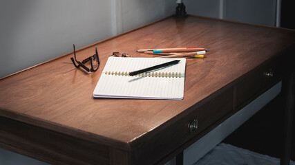 Close-up from a high angle of a white notepad next to a few wooden colorful pencils on a oak desk with a warm light over them.