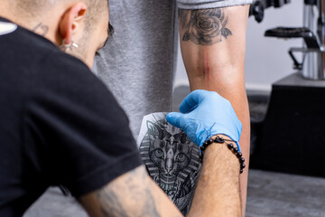 Tattoo artist removing the tracing paper from a leg in a tattoo studio.
