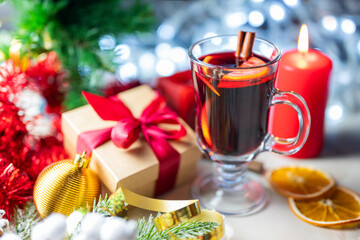 delicious hot spicy red mulled wine with orange and cinnamon spices near the Christmas tree with decorations and bokeh garlands