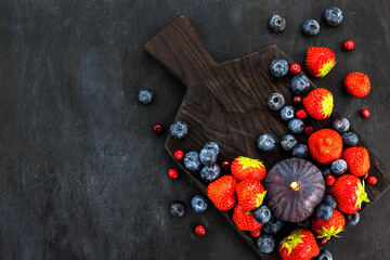 Fresh strawberries, blueberries and figs, on dark background, top view