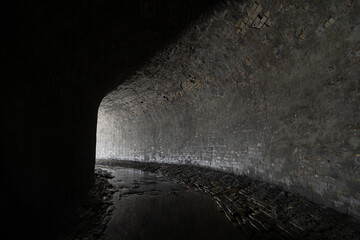 Old brickwork sewer tunnel with light from the turn. Underground river or old rainwater collector...