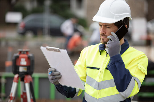contractor on site looking at clipboard and talking on smartphone