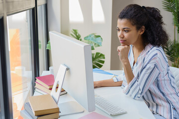 Pensive African American businesswoman using computer searching online sitting in modern office....