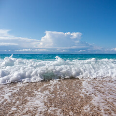 Shining white foam droplet on pebble beach with waves and epic clouds on coast of Lefkada island in Greece. Summer nature of Ionian Sea