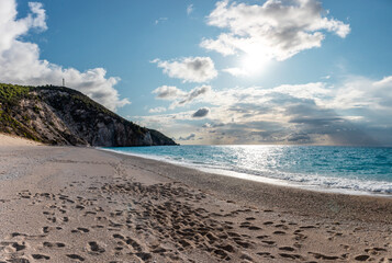 Sun and clouds above warm Mylos beach shore on sunny coast with high cliffs and blue seascape. Lefkada island in Greece. Summer travel to Ionian Sea