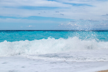 Azure breaker waves with white foam hitting shore. Coast of Greek island with blue sky. Sandy beach in Greece. Summer nature travel to Ionian Sea